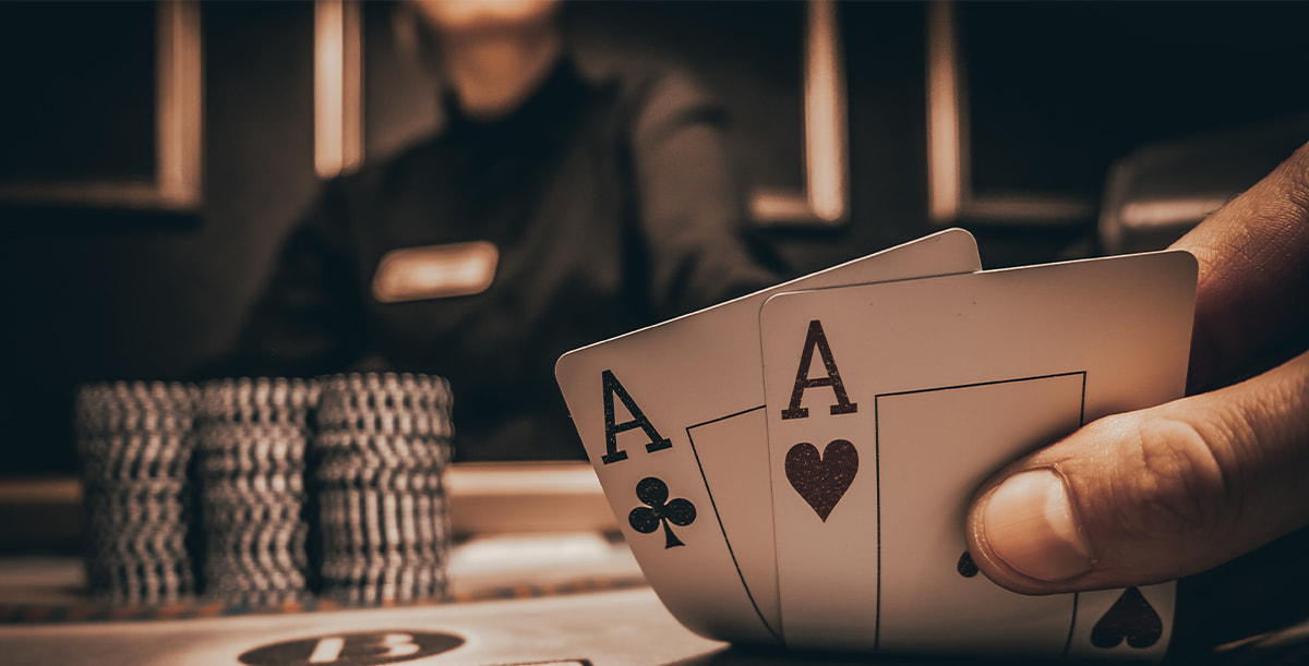 Zwei Asse als Startkarten auf einem Pokertisch, umgeben von bunten Chips, während andere Spieler sich auf ihre Karten konzentrieren.