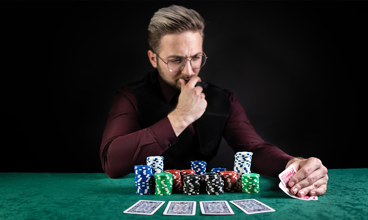 Ein Mann sitzt an einem Pokertisch und schaut sich konzentriert seine Karten an. 