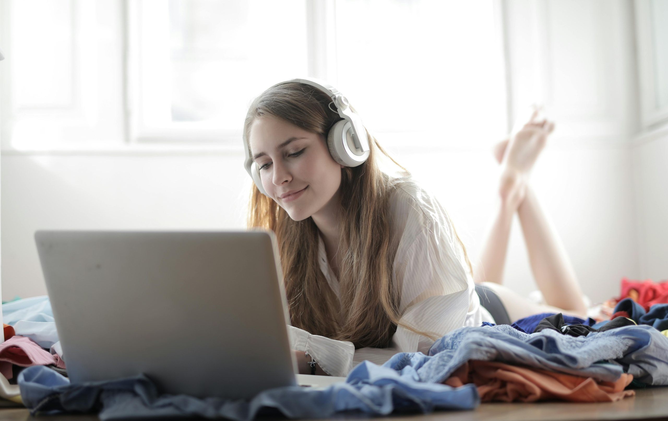 Frau mit Kopfhörern liegt mit Laptop auf einem Bett.