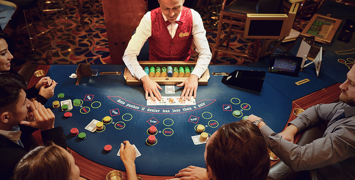 Mehrere Personen sitzen in an einem Pokertisch mit Pokerchips & Karten vor ihnen.