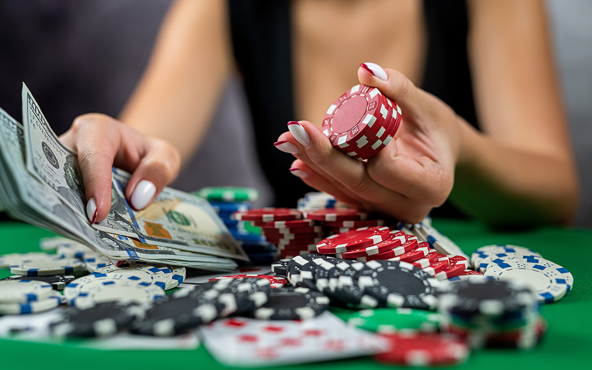 Eine weibliche Person sitzt vor einem Pokertisch mit vielen Pokerchips und Karten und hält eine Menge Geldscheine in der Hand.